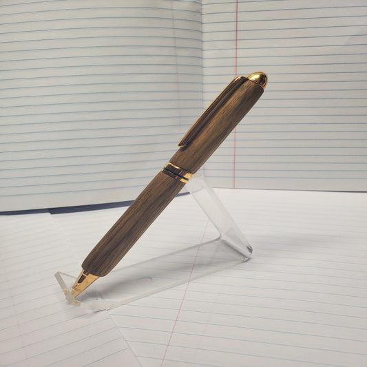 Black Limba wood pen with gold accents on a clear stand against a lined paper background